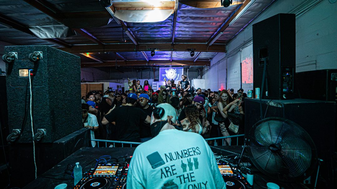 NOWHERE INC. seen from behind at the decks, facing a packed warehouse crowd